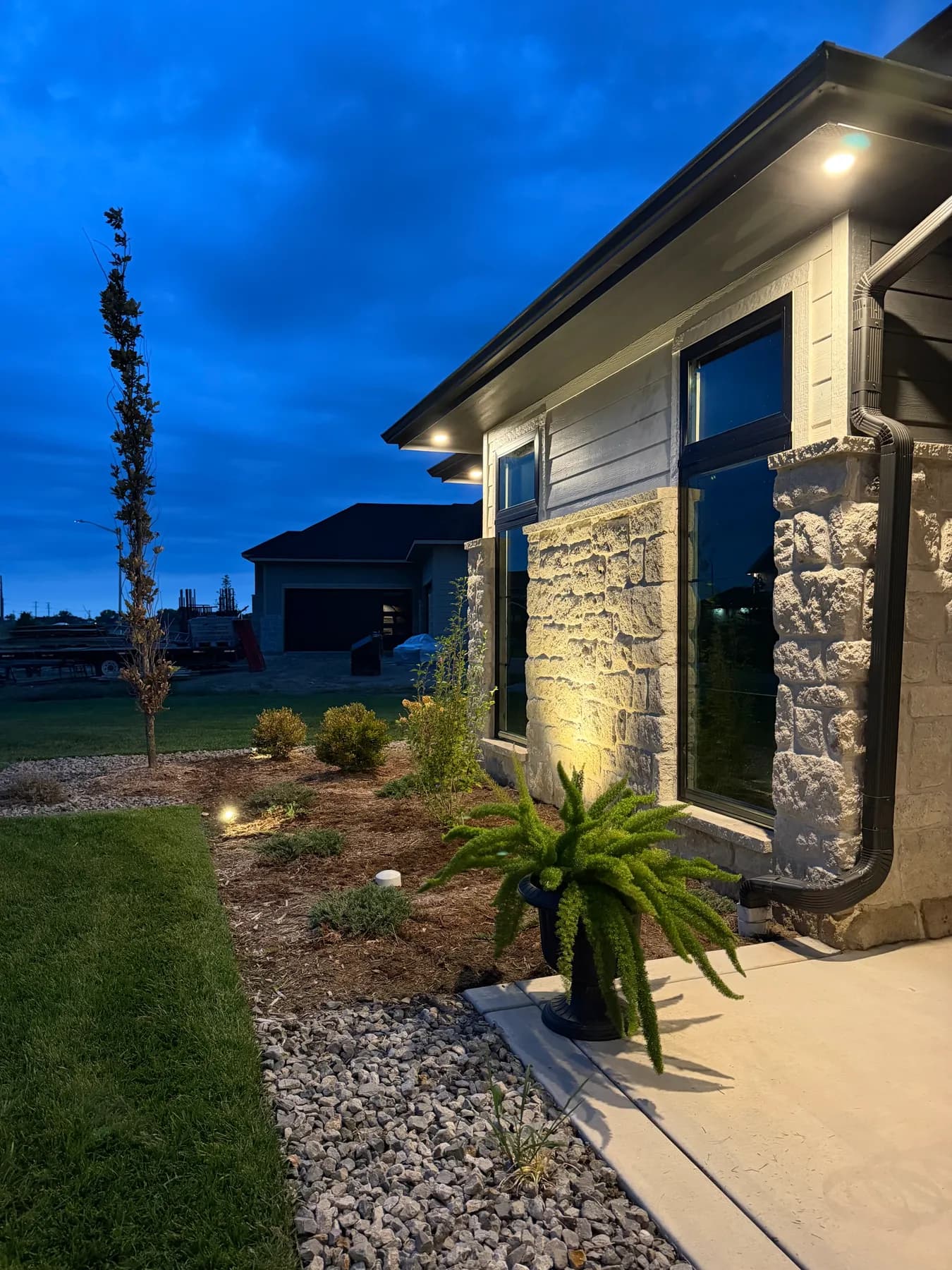 Entry plantings and stone column lit at dusk in the Coves