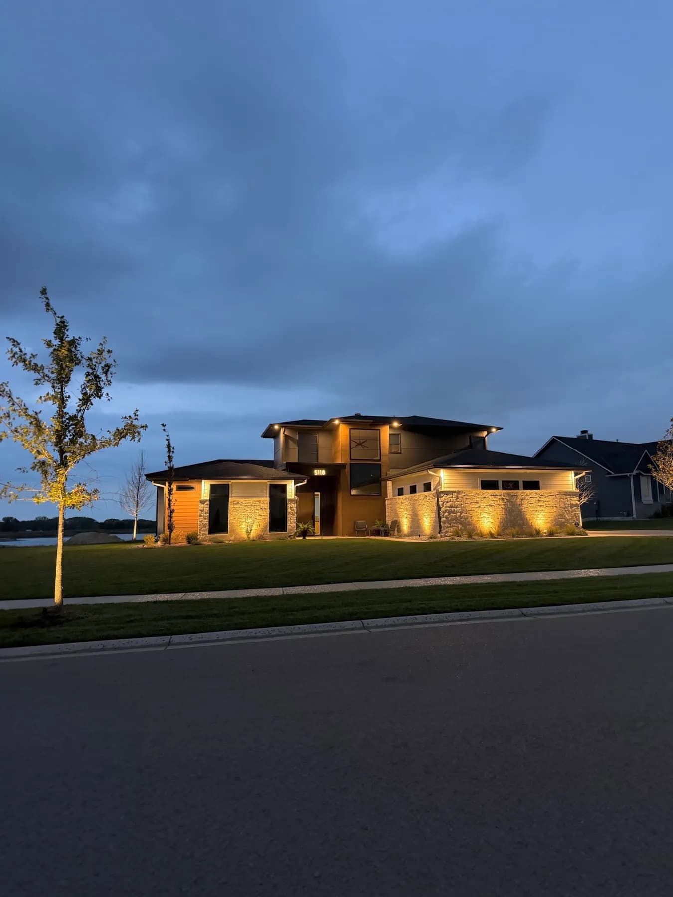 Street view of a lit modern home and uplit young tree in the Coves